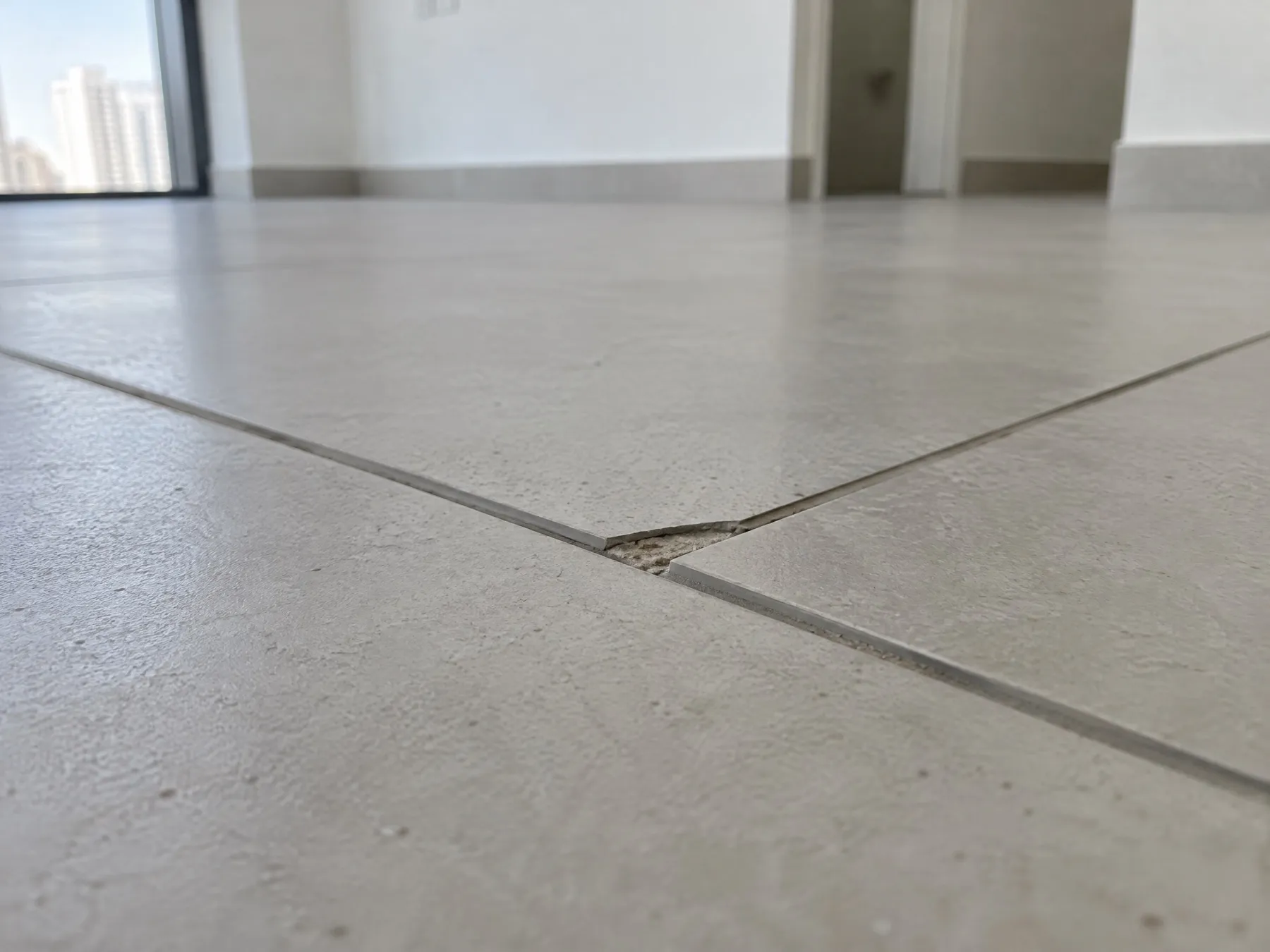 A chipped edge on a large light grey porcelain floor tile, at the joint with the next tile