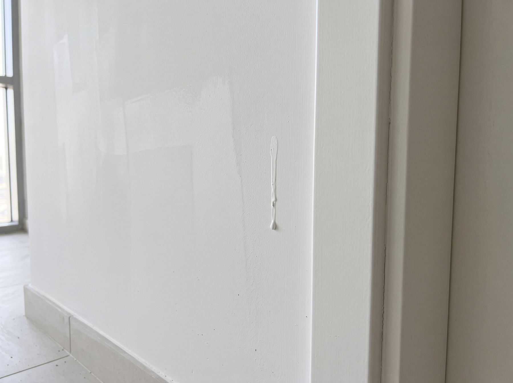 A dried paint drip on a white wall next to a door frame, circled in red.