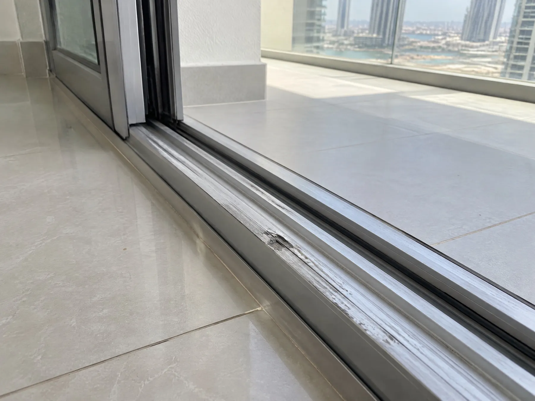 Scrapes and a gouge along an aluminium sliding door track at a balcony threshold