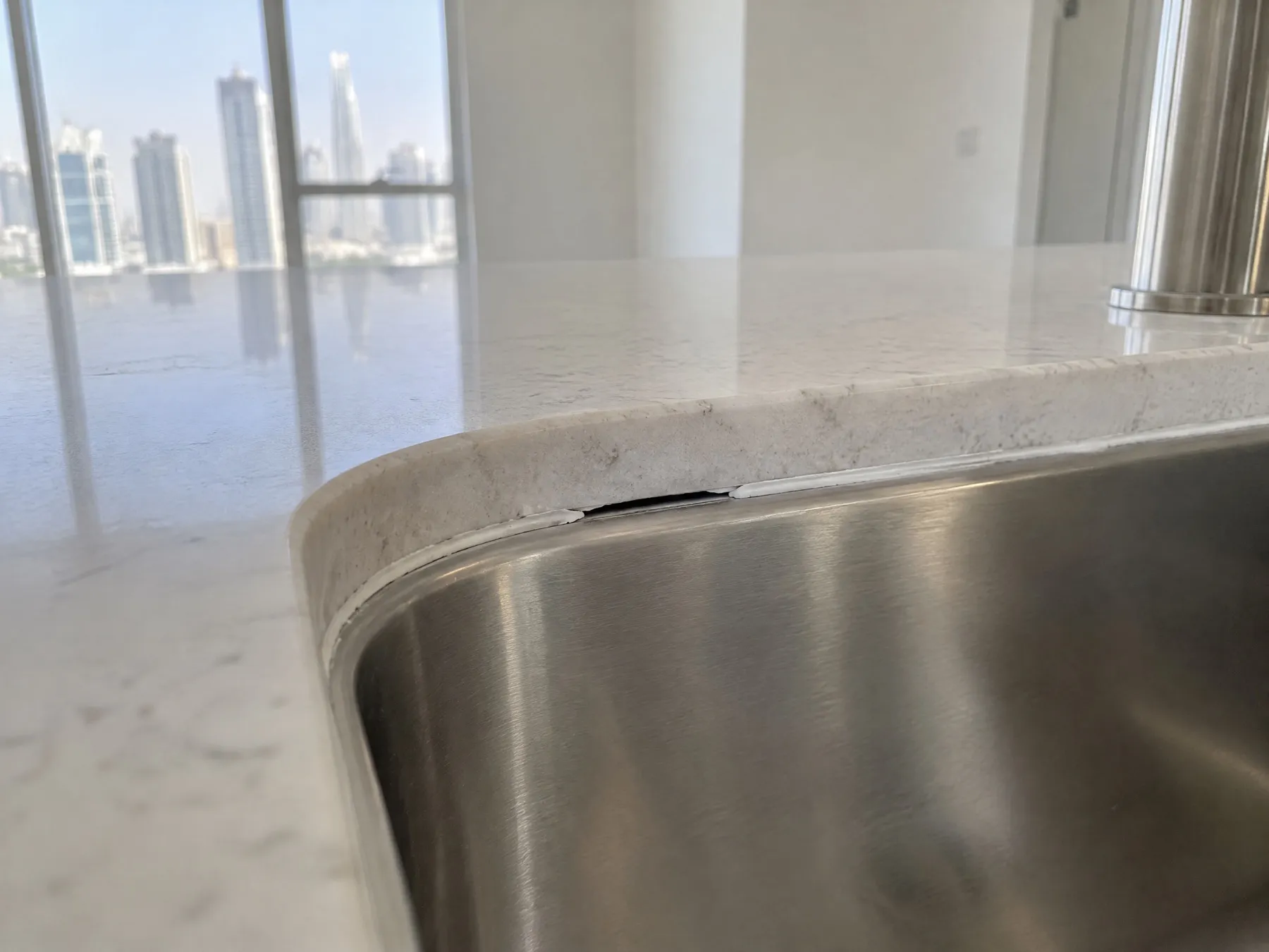 A gap in the white silicone bead where a stainless steel sink meets a stone worktop